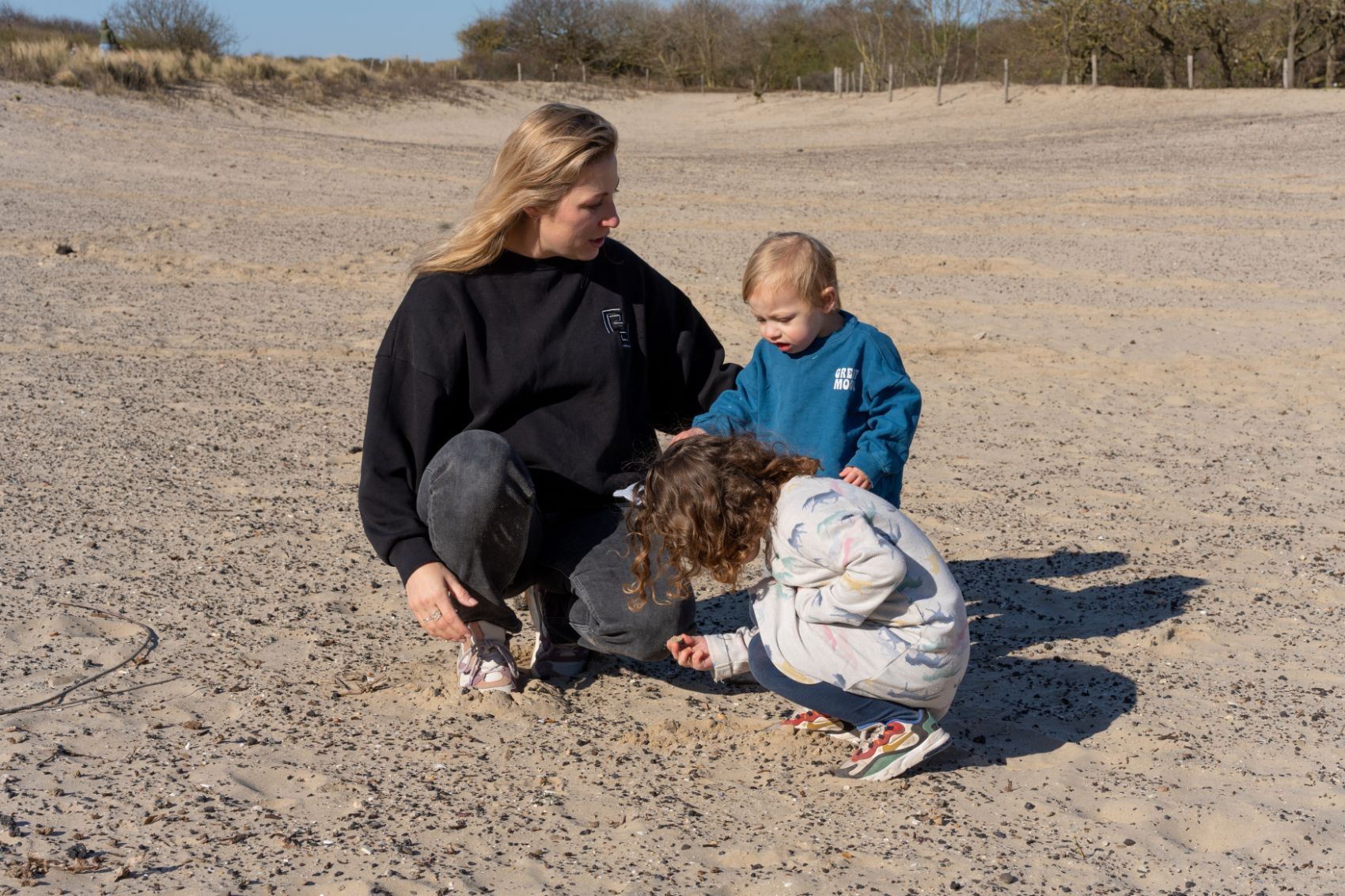 Moeder speelt met kinderen in de duinen